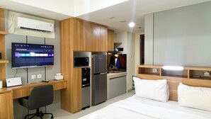 A hotel room with a bed, desk, kitchenette, and a TV mounted on the wall. - Minimalist Design Studio At Pollux Chadstone Apartment (Cikarang)