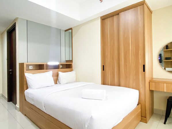 A bedroom with a bed, wooden wardrobe, and a mirror. - Minimalist Design Studio At Pollux Chadstone Apartment (Cikarang)