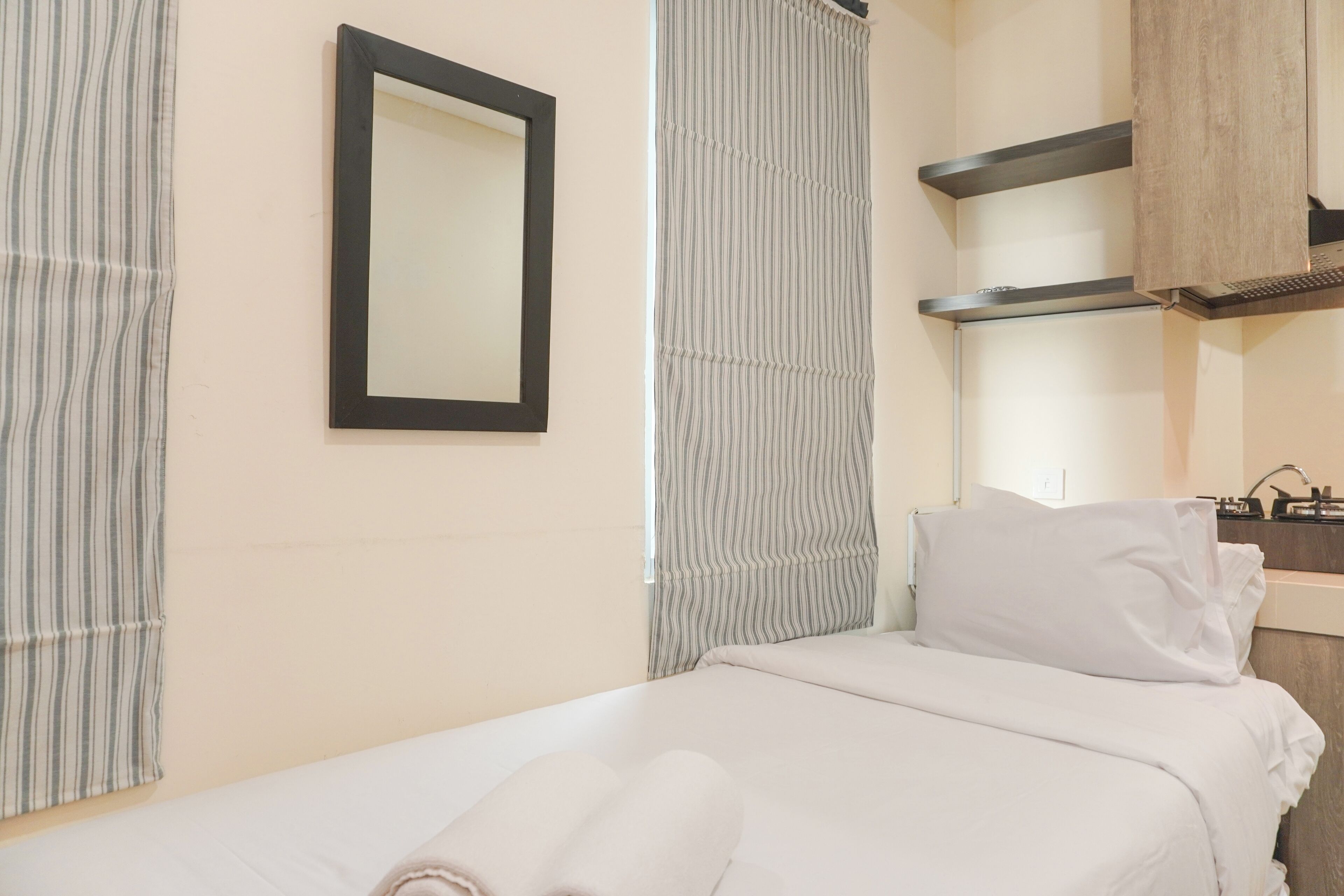 A hotel room with a bed, a mirror, a window with curtains, and a wooden cabinet.