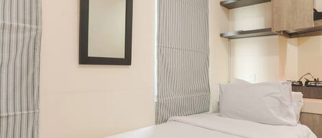 A hotel room with a bed, a mirror, a window with curtains, and a wooden cabinet.