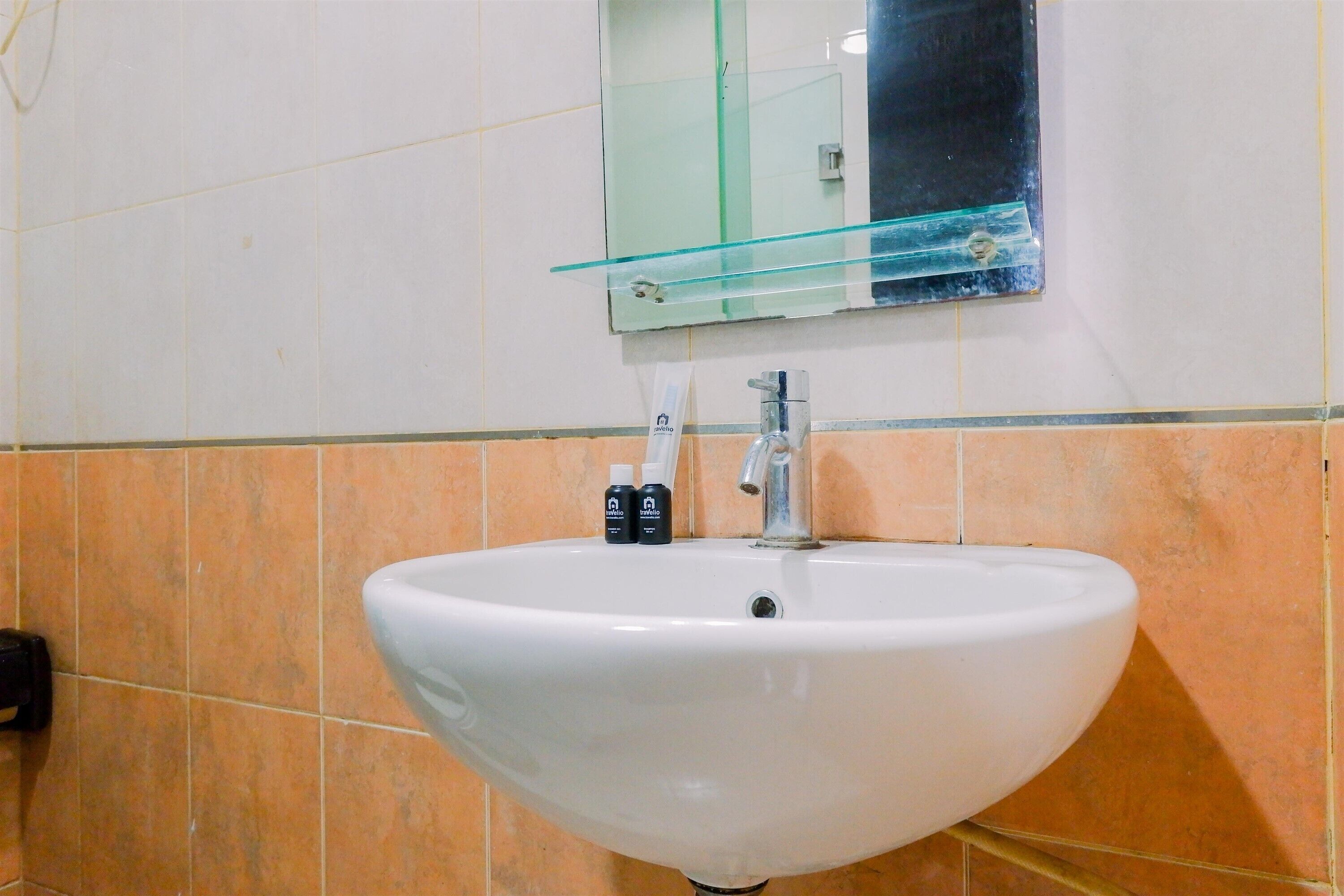 A white sink with a glass shelf above it, a mirror, and orange-tiled walls.