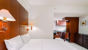 A hotel room with a large bed, two bedside lamps, a wooden wardrobe, and a small kitchenette. - Good Deal And Restful Studio Tamansari Sudirman Apartment (Jakarta)