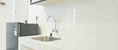 A modern kitchen with white tiles, a stainless steel sink, and a built-in refrigerator.