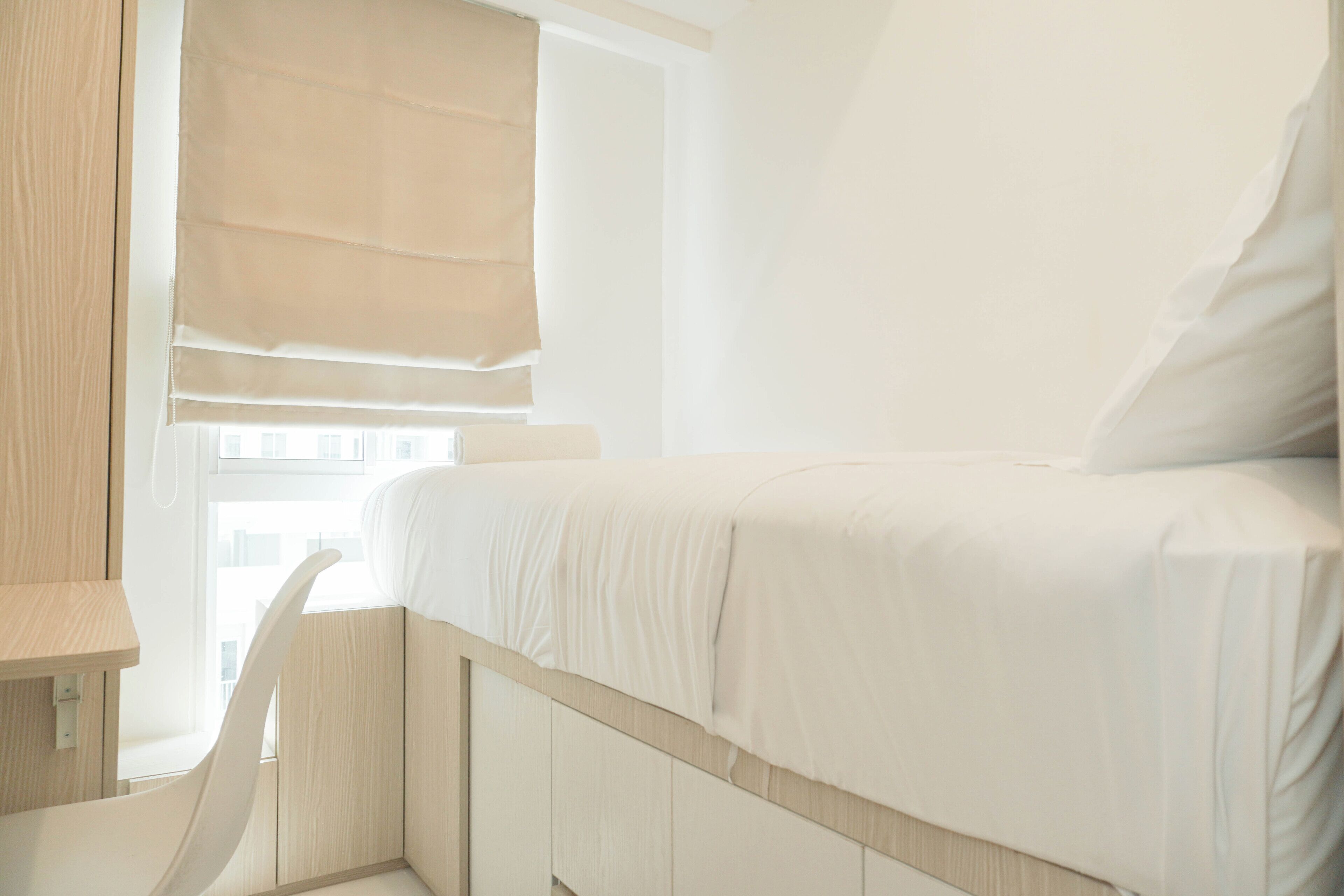 Moderni hotellihuone, jossa on sänky, työpöytä ja ikkuna, jossa on sälekaihtimet.