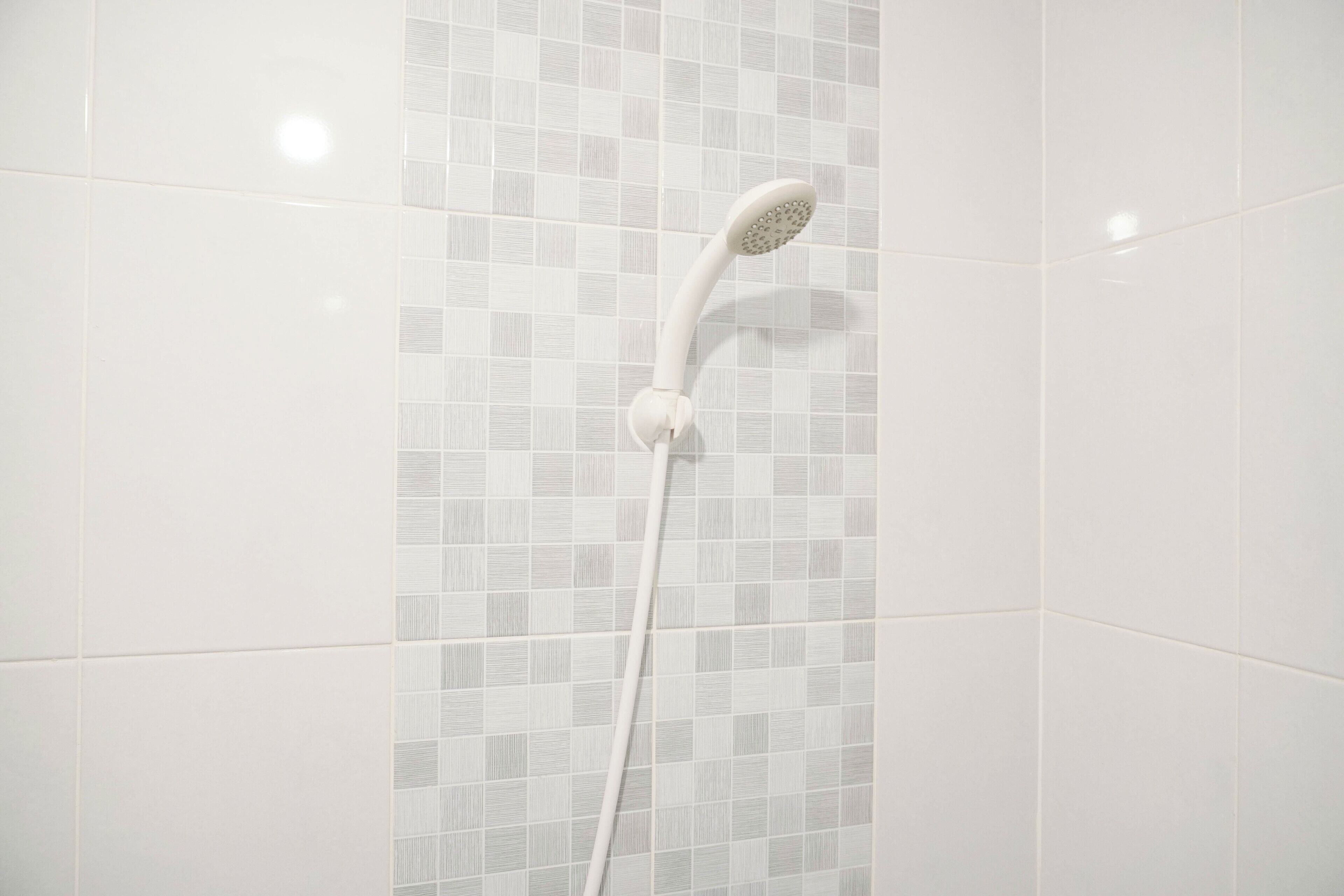 A shower with a curved head and a white handle against a tiled wall.