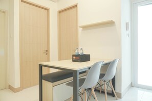 A small, clean room with a wooden door, a white table with two chairs, and a shelf above the table. - Comfy And Good 2Br Tokyo Riverside Pik 2 Apartment (Teluknaga)