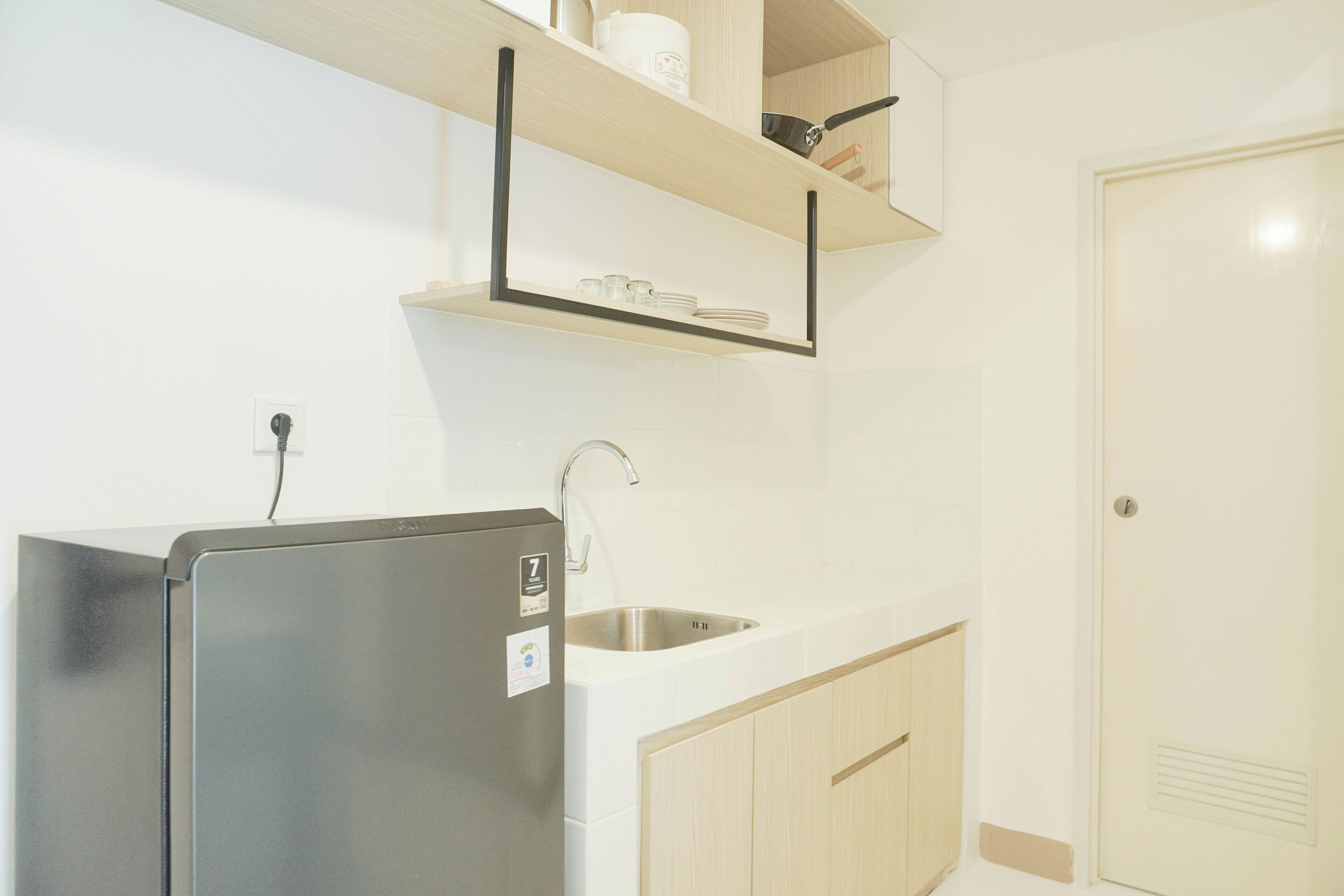 A compact kitchen with a stainless steel refrigerator, a sink, and wooden cabinets.