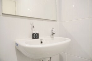 A white bathroom sink with a mirror above it and two bottles of toiletries on the sink. - Comfy And Good 2Br Tokyo Riverside Pik 2 Apartment (Teluknaga)