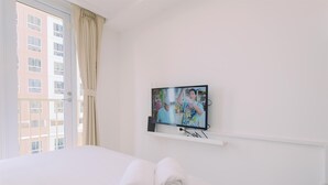 Et hotelværelse med en seng, et fjernsyn ophængt på væggen og et vindue med gardiner.