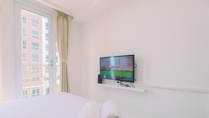 Et hotelværelse med en seng, et fjernsyn ophængt på væggen og et vindue med gardiner.