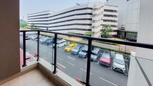 A view from a balcony overlooking a parking area with several cars, a multi-story building, and a clear sky.