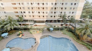 A hotel courtyard with two swimming pools, palm trees, and outdoor seating. - Good Deal And Comfy 2Br Kebagusan City Apartment (Jakarta)