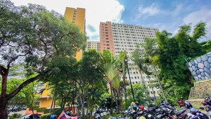 A parking area with multiple motorcycles, surrounded by trees and buildings, including a tall hotel. - Good Deal And Comfy 2Br Kebagusan City Apartment (Jakarta)