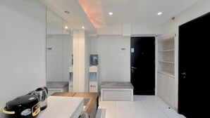 A modern hotel room with a kitchenette, a water dispenser, a bench, and a black wardrobe. - Good Deal And Comfy 2Br Kebagusan City Apartment (Jakarta)