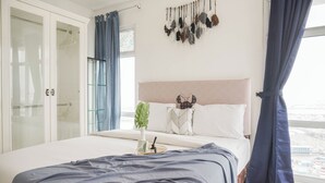 Une chambre à coucher avec un lit, une table de chevet ornée d’une plante, une décoration suspendue et une vue sur la ville par la fenêtre.
