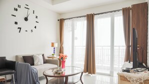 Un salon doté d  ’une grande horloge murale, d’un canapé, d’une table basse agrémentée d’objets décoratifs et offrant une vue sur l’extérieur grâce à de grandes fenêtres.