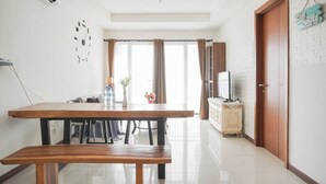 Un coin repas avec une table et un banc en bois, un téléviseur posé sur un meuble et une horloge murale.