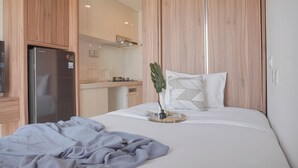 A modern bedroom with a bed, a small desk, and a refrigerator. - Comfortable And Good Place Studio At Sky House Bsd Apartment (Pagedangan)