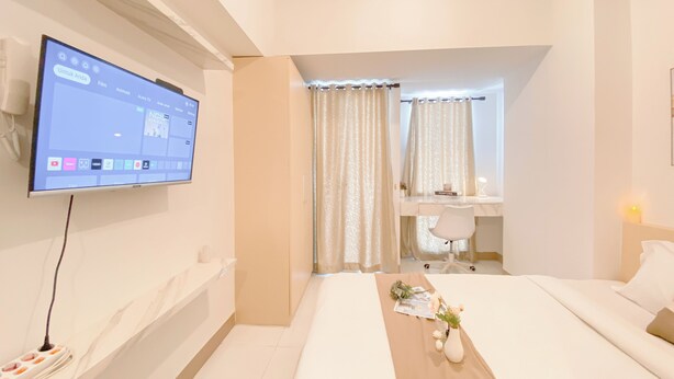 Ein modernes Hotelzimmer mit einem an der Wand befestigten Flachbildfernseher, einem Bett mit Holz-Kopfteil, einem Schreibtisch mit Stuhl und einem kleinen Tisch mit Blumenvase.