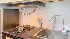 A kitchen with a black stove, a stainless steel sink, and a white tiled backsplash.