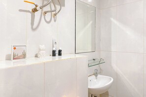 Een badkamer met witte tegels, een glazen plankje, een wastafel, een spiegel en een douche met een handdouche.