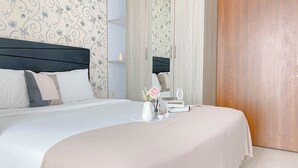 A neatly made bed with a white and beige bedspread, a vase with flowers, and a small table with a candle and a book.