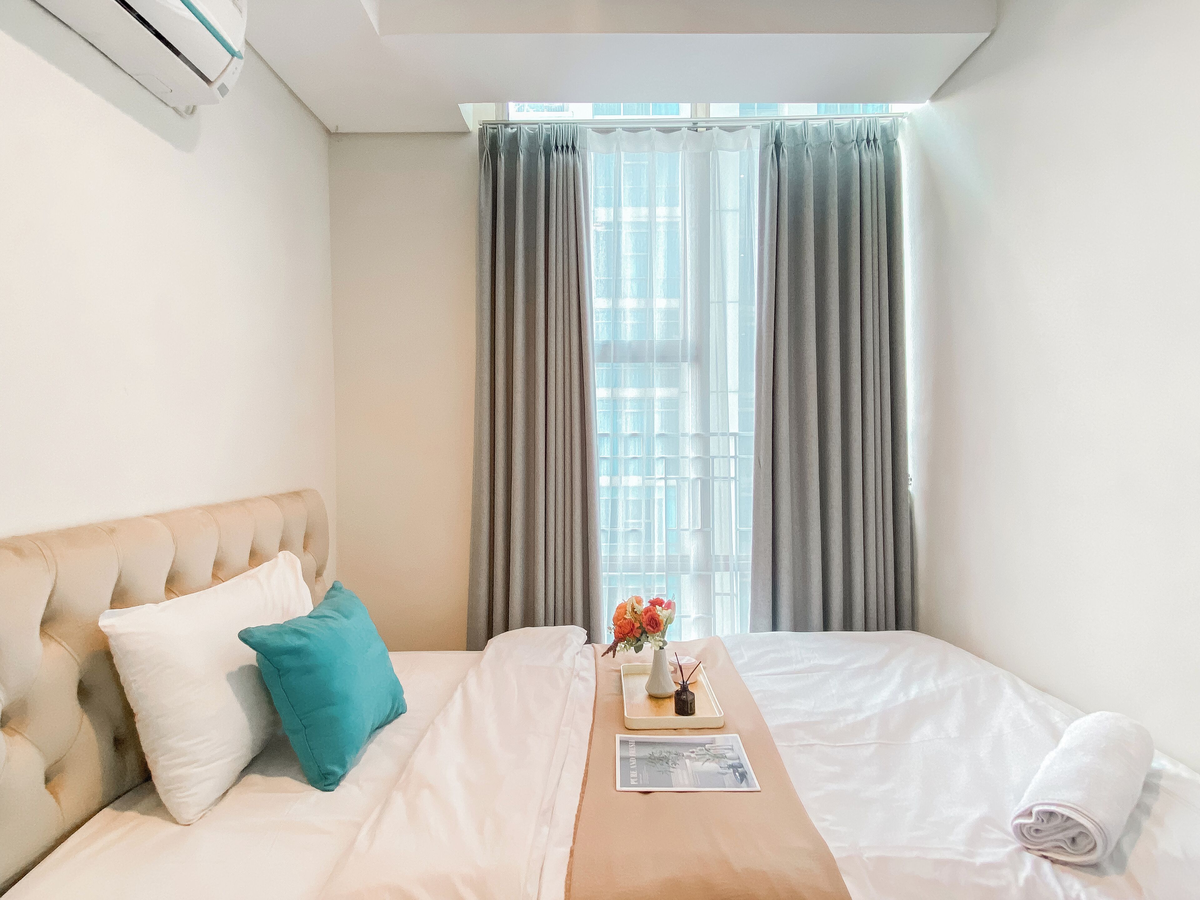 A hotel room with a bed, a bedside table with a vase of flowers, and a window with curtains.