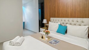 Una habitación de hotel moderna con una cama grande, ropa de cama blanca, cabecera de madera, mesita de noche con lámpara y un pequeño jarrón con flores.