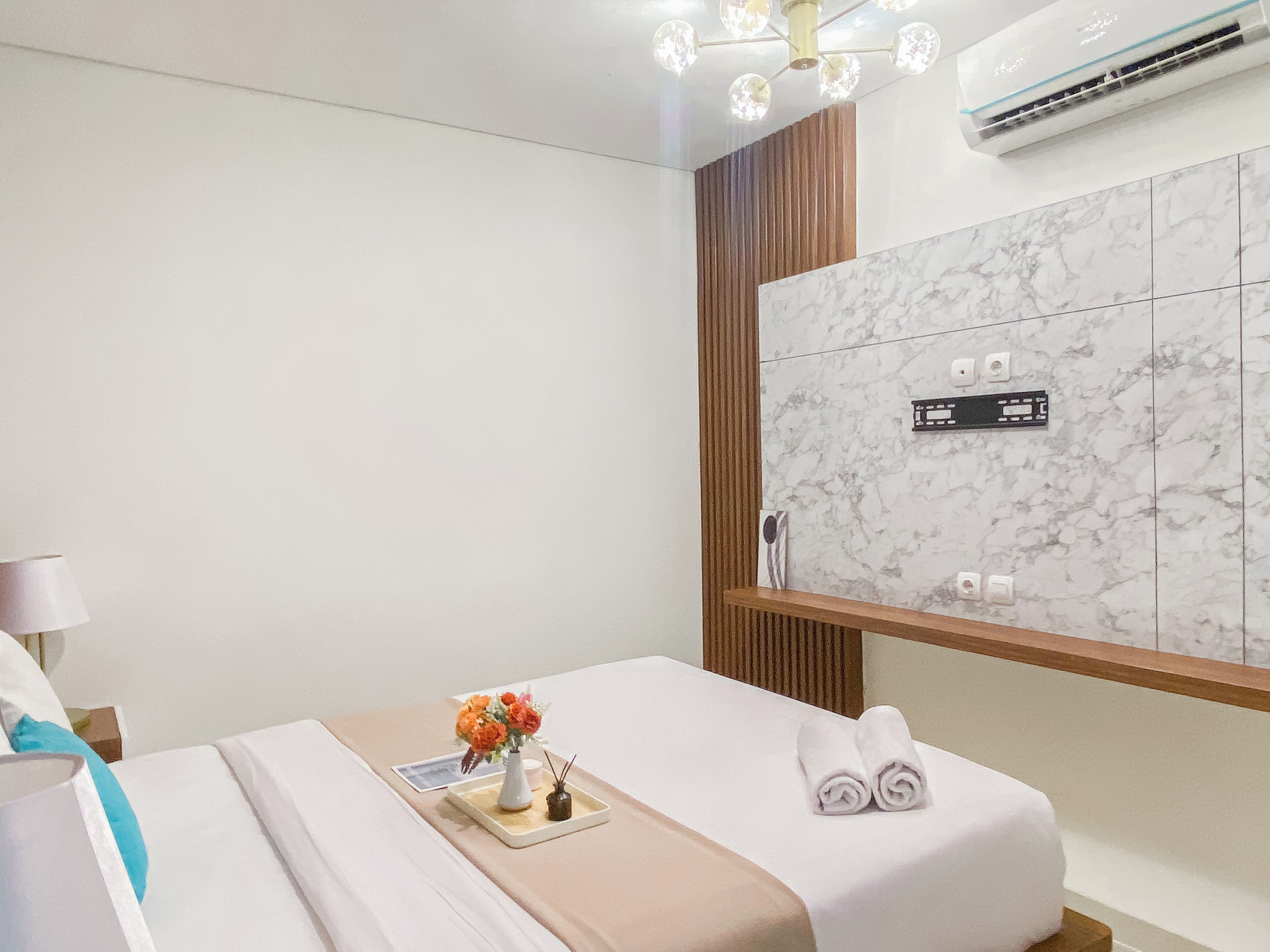 A modern hotel room with a marble wall, a wooden panel, and a bed with a white bedspread and towels.