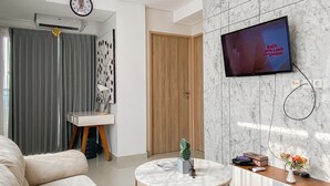 Una sala de estar moderna con un televisor de pantalla plana montado en una pared de mármol, una mesa redonda, un sofá y una puerta que da a otra habitación.