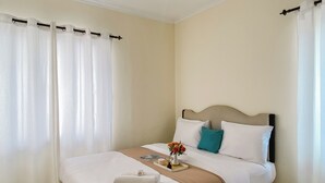 A neatly made bed with a beige headboard, white bedding, and a teal pillow. There is a small vase with flowers on the bed. - Homey And Modern 2Br At Marina Ancol Apartment (Jakarta)