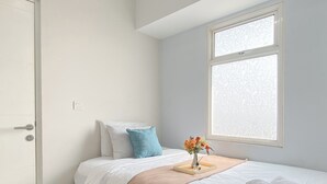 A bedroom with a bed, a window, a door, and a bedside table with a vase of flowers. - Comfort Living 2Br Springlake Summarecon Bekasi Apartment (Bekasi)