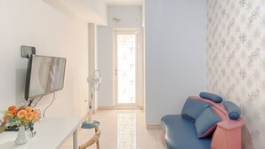 A modern living room with a flat-screen TV, a blue and pink sofa, a white desk with a vase of flowers, and a patterned wall. - Comfort Living 2Br Springlake Summarecon Bekasi Apartment (Bekasi)