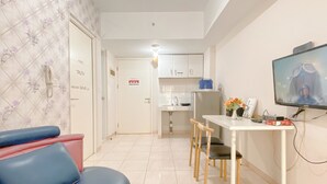 A modern living room with a blue sofa, a dining table with chairs, a kitchen area, and a TV mounted on the wall. - Comfort Living 2Br Springlake Summarecon Bekasi Apartment (Bekasi)