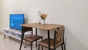 A small room with a wooden table, two chairs, a TV on a stand, and a vase with flowers.
