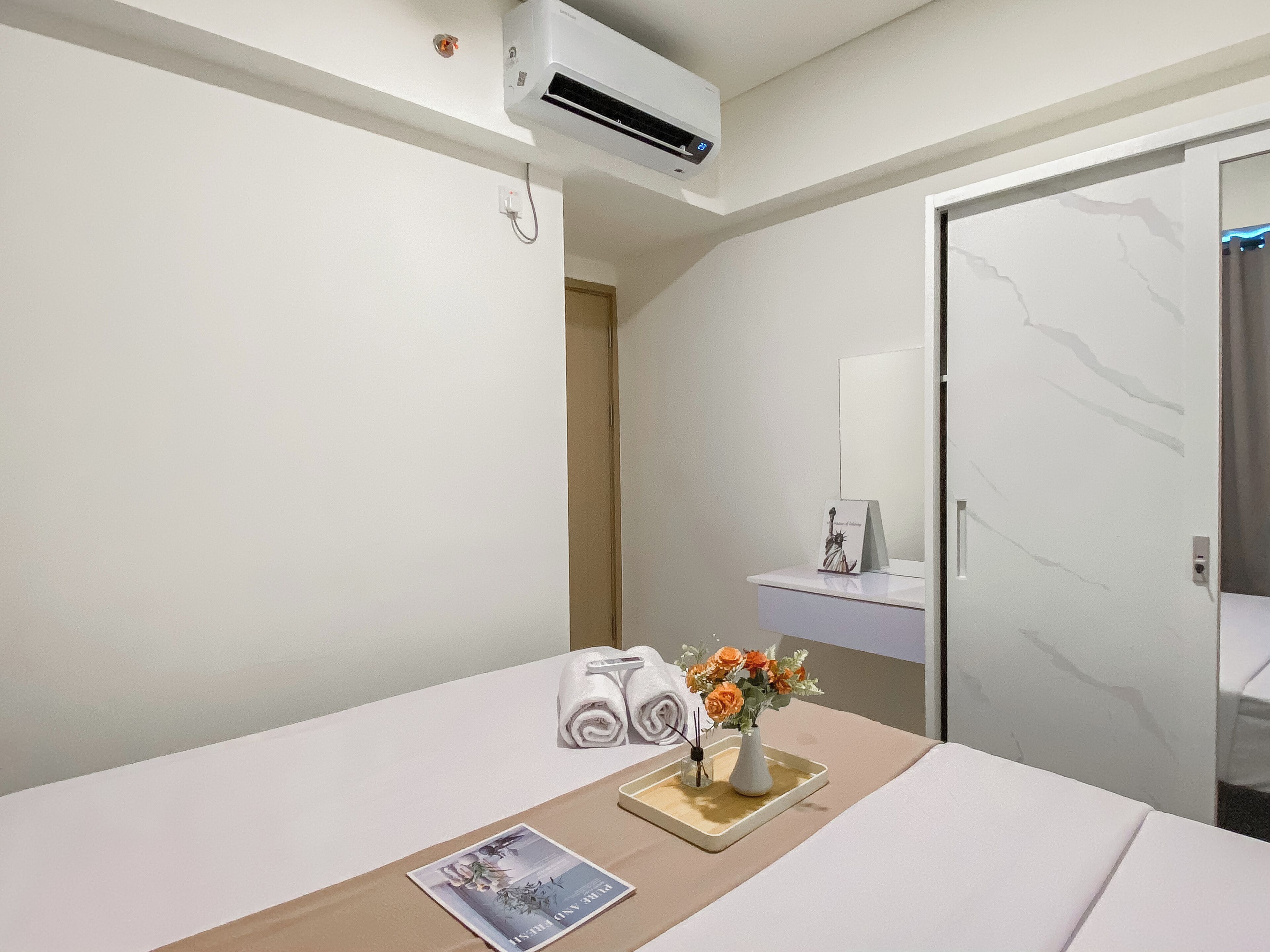 A hotel room with a bed, a bedside table with a vase of flowers, a towel, and a small card.