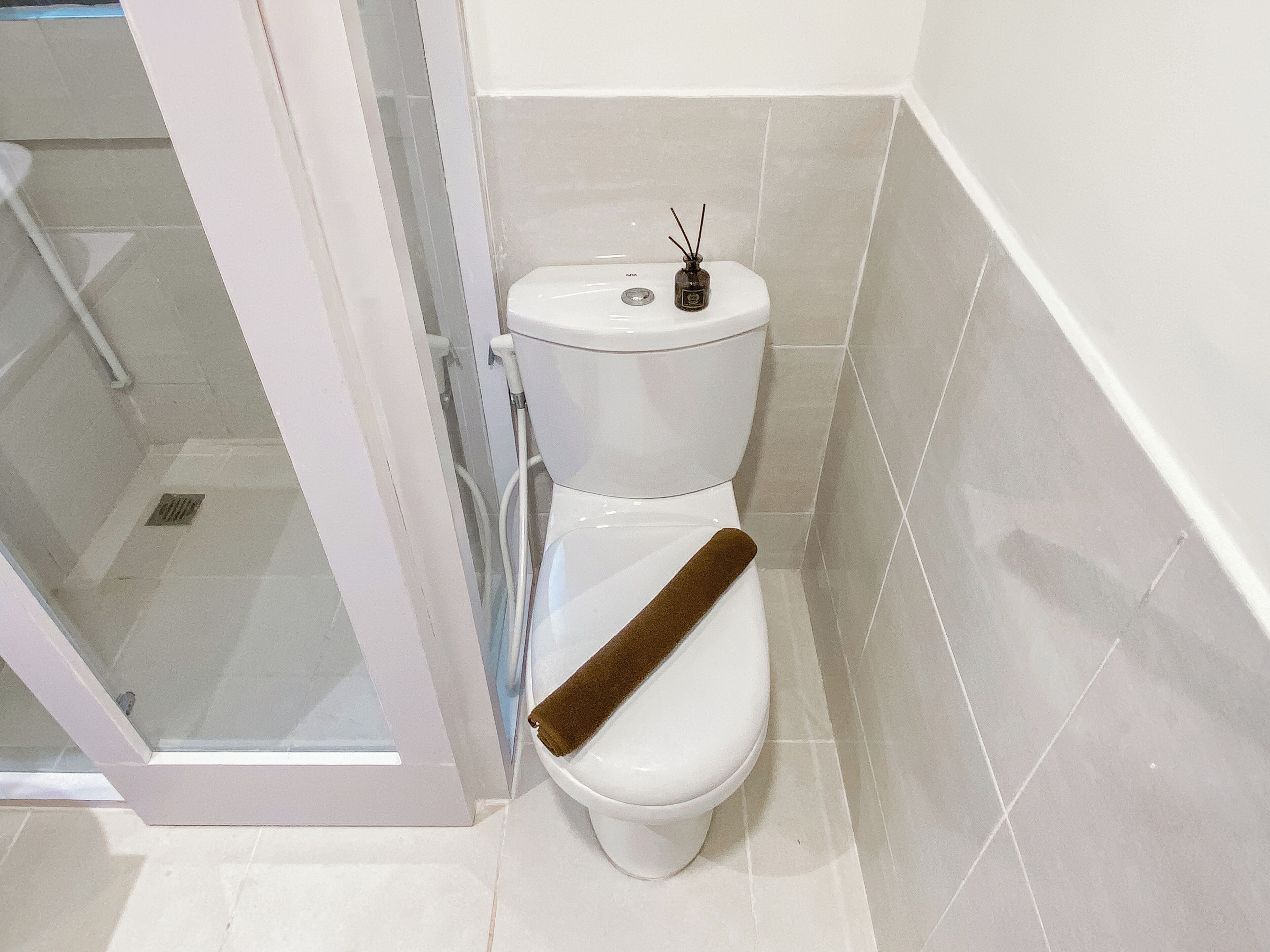 Une salle de bain équipée de toilettes, d’une douche à parois de verre et de murs carrelés.