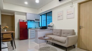 A modern kitchen with a red refrigerator, a dining table with chairs, a sofa, and a small round table with a lamp.