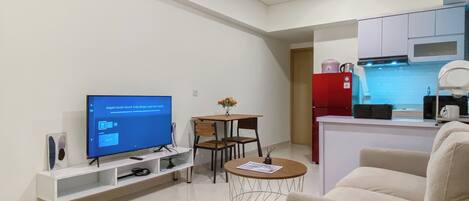 Una sala de estar moderna con televisor, sofá, mesa de centro y comedor con sillas y una mesita.