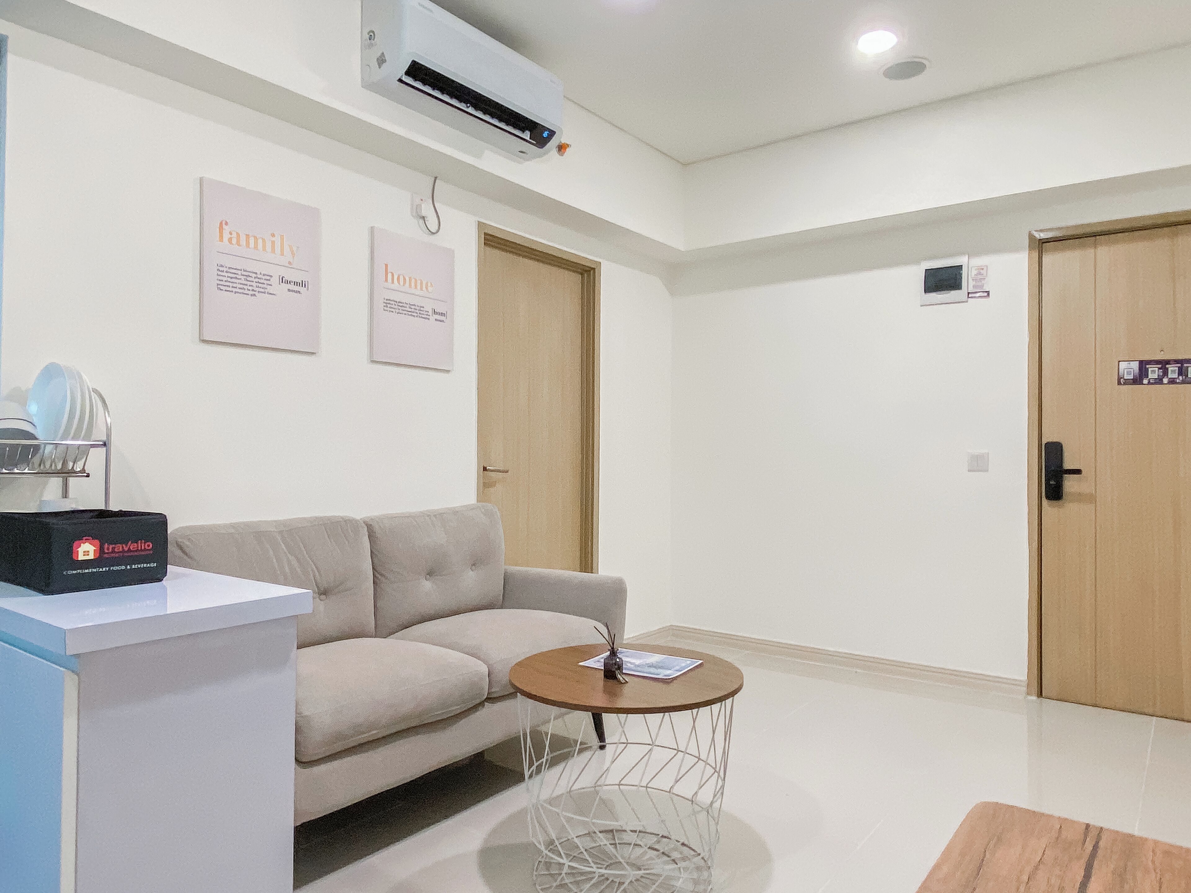 Habitación de hotel moderna con sofá, una pequeña mesa redonda, equipo de aire acondicionado y dos letreros enmarcados en la pared.