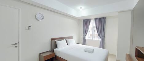 A modern bedroom with a bed, bedside table, and a clock on the wall.