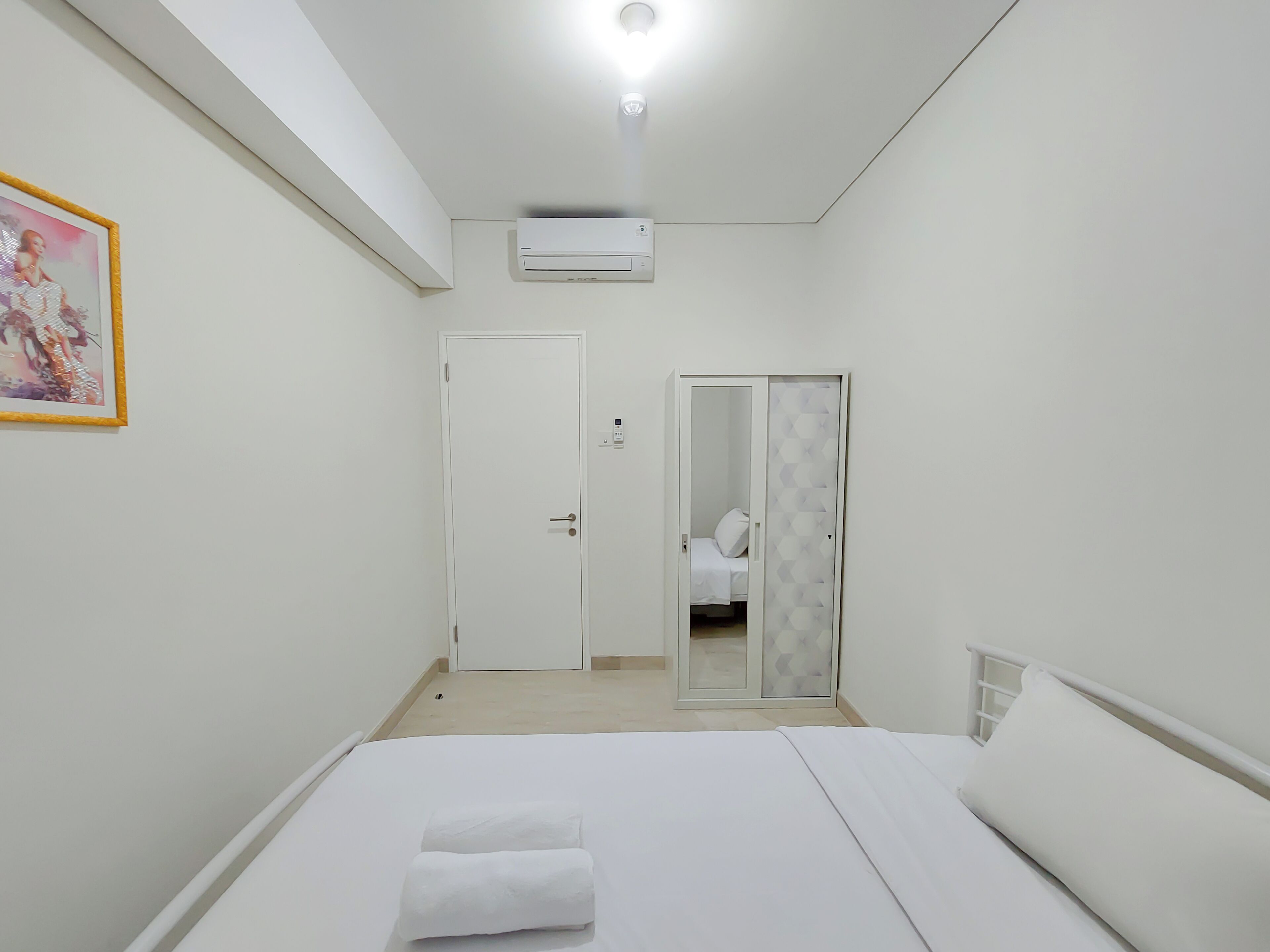 A hotel room with a bed, a bedside table, a wardrobe, and a bathroom visible through a door.