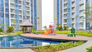A residential area with high-rise buildings, a children's play area, and a swimming pool. - Good Place And Homey 2Br At Podomoro City Deli Medan Apartment (Medan)