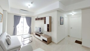 A modern, well-lit living room with a sofa, a coffee table, a TV, and built-in shelving. - Good Place And Homey 2Br At Podomoro City Deli Medan Apartment (Medan)