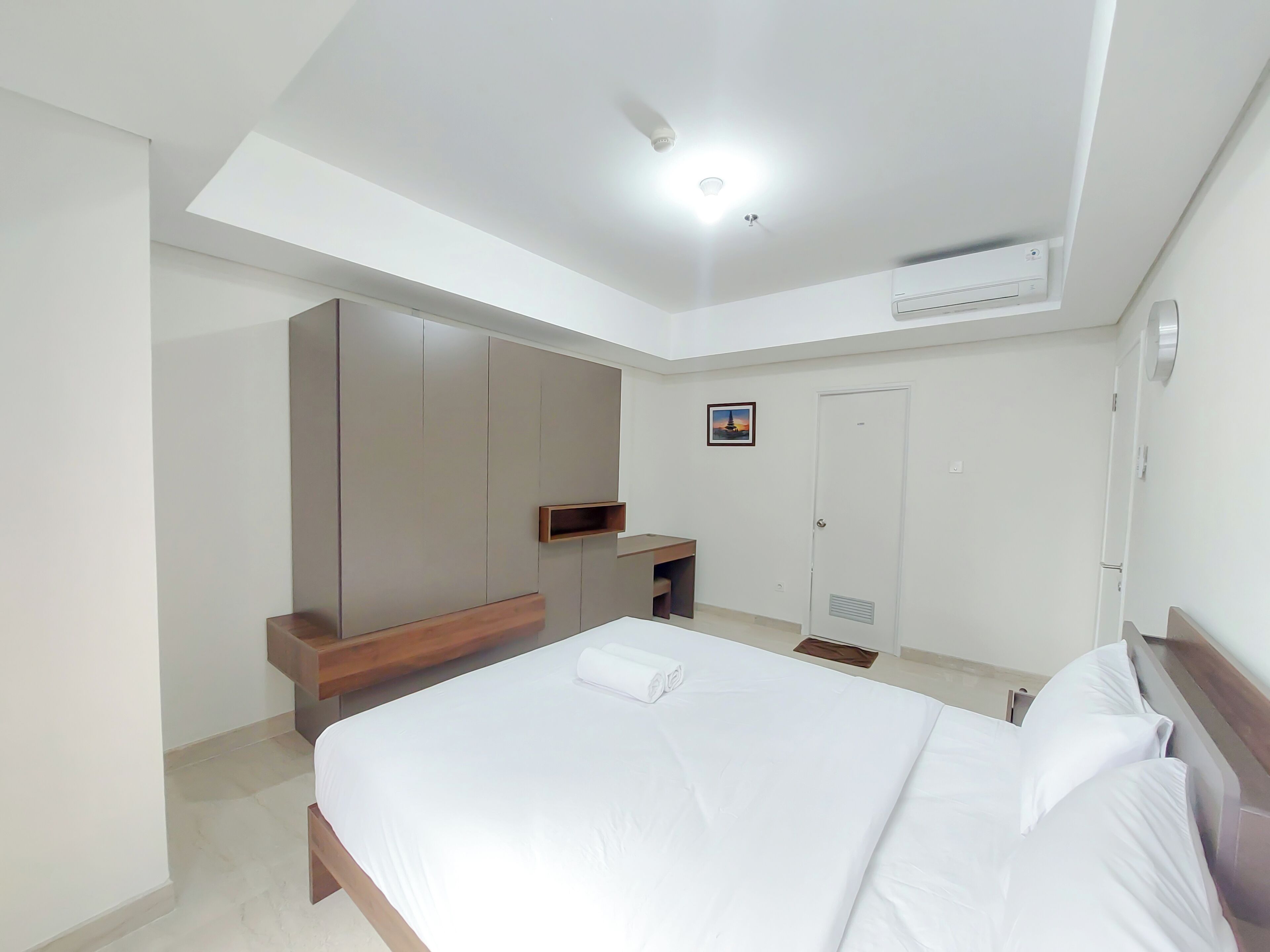 A modern hotel room with a large bed, built-in wardrobe, and a small desk.