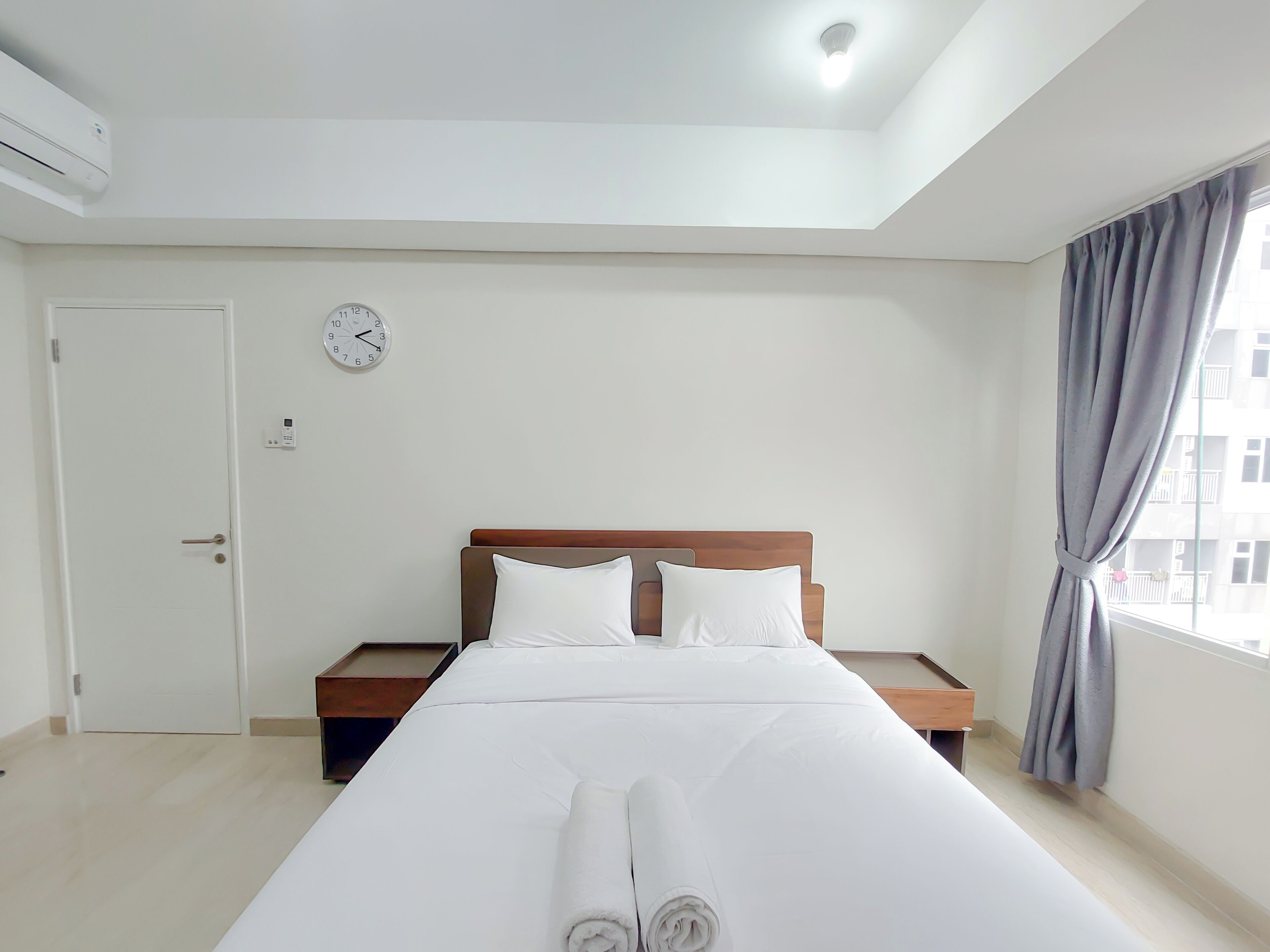 A hotel room with a bed, a bedside table, a clock, and a window with curtains.
