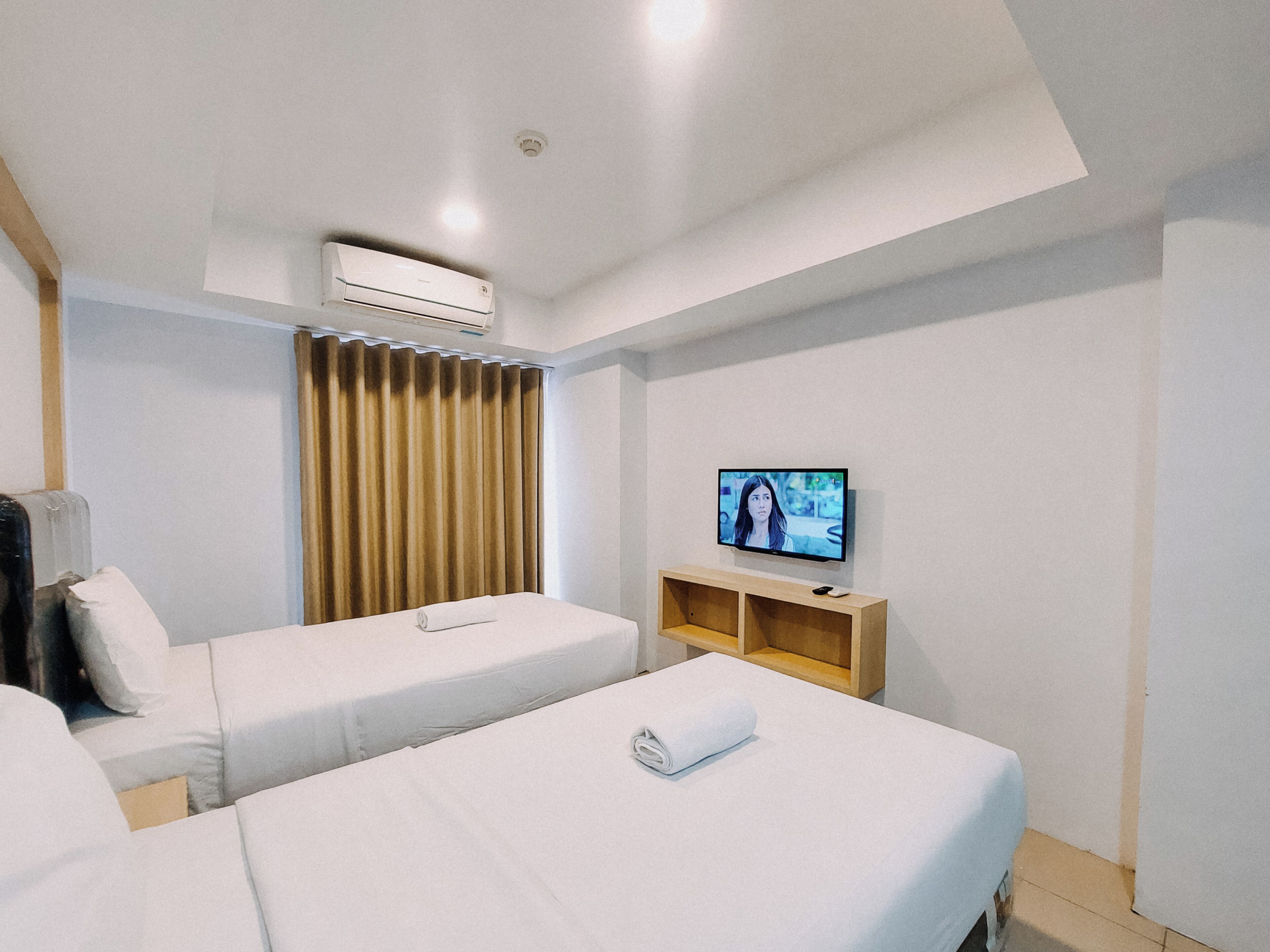 A hotel room with two beds, a TV, an air conditioning unit, and a wooden shelf.