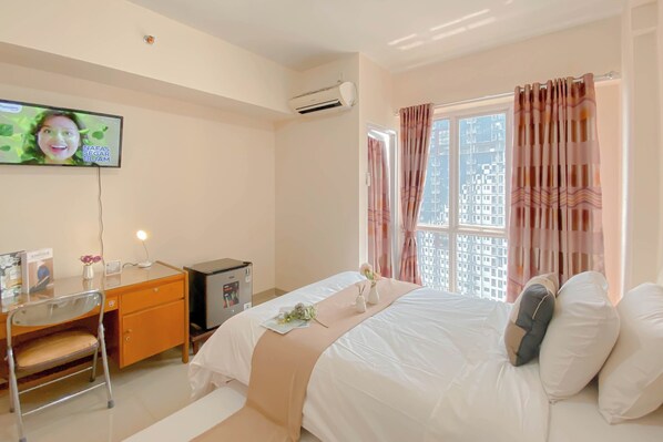 Una habitación de hotel con cama, escritorio, silla, televisor y ventana con cortinas.