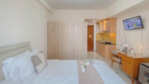 Una habitación de hotel con cama, escritorio, silla, televisor y kitchenette.