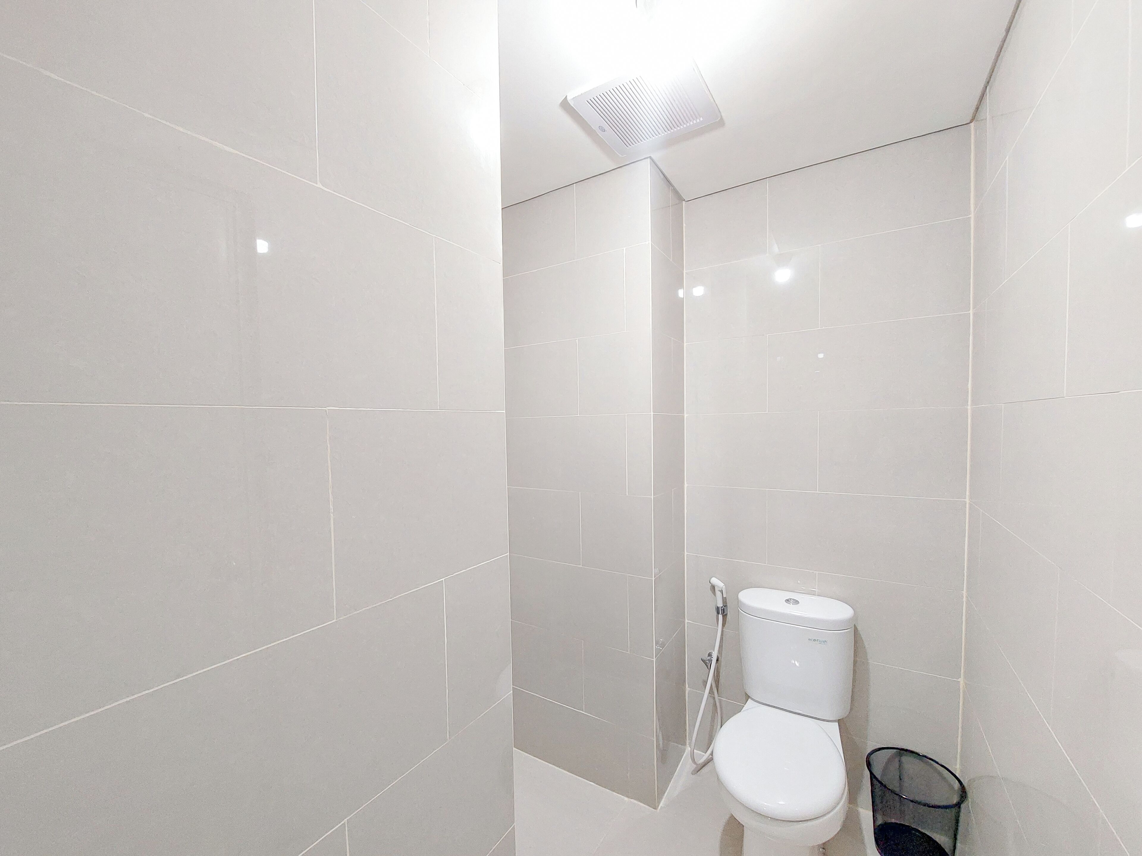 Un baño moderno con azulejos blancos, un inodoro, una ducha y un cubo de basura de vidrio.
